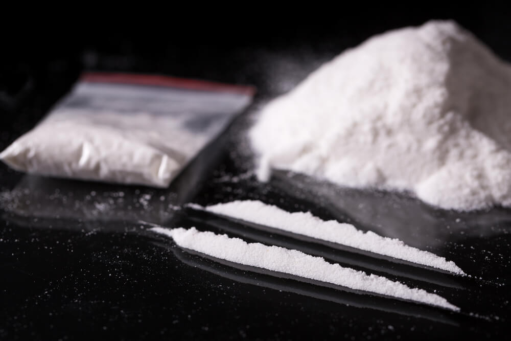 two lines of cocaine on a black table with a bag and large pile in the background